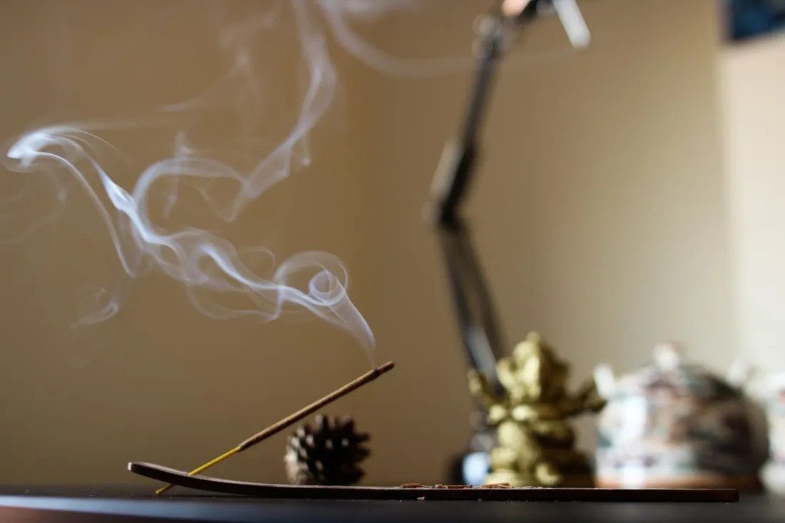 Incense smoke curling upward in the quiet healing room, a small brass statue in the warm light behind
