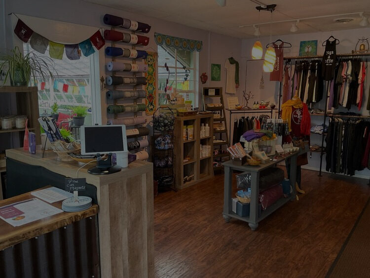 Inside the Taproot Yoga shop: racks of rolled mats, cozy clothing, and prayer flags over the window
